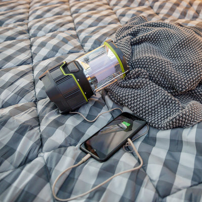Image of lantern laying on sleeping bag with smart phone plugged in for device charging