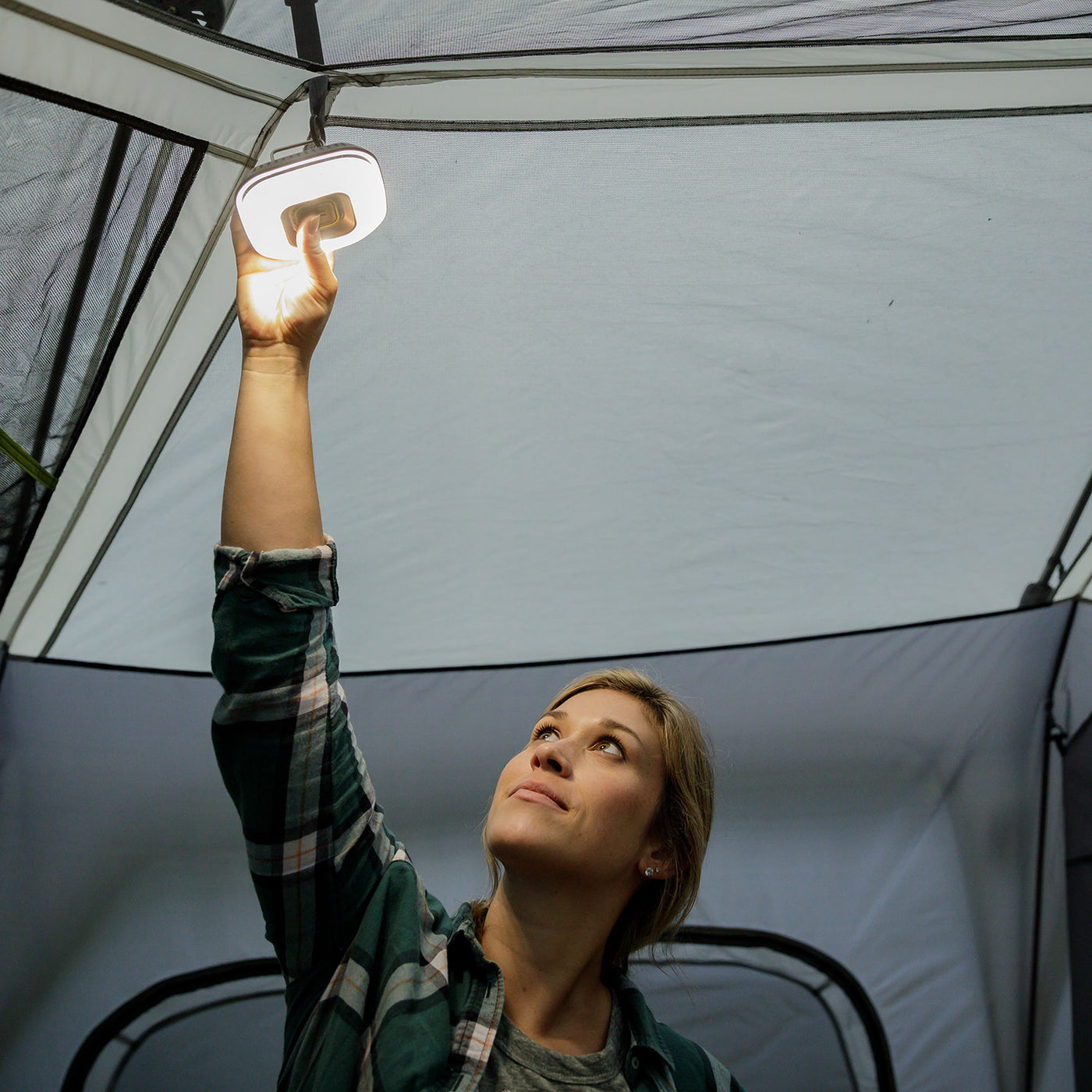 Lifestyle image of woman hanging tent light on tent ceiling with light on
