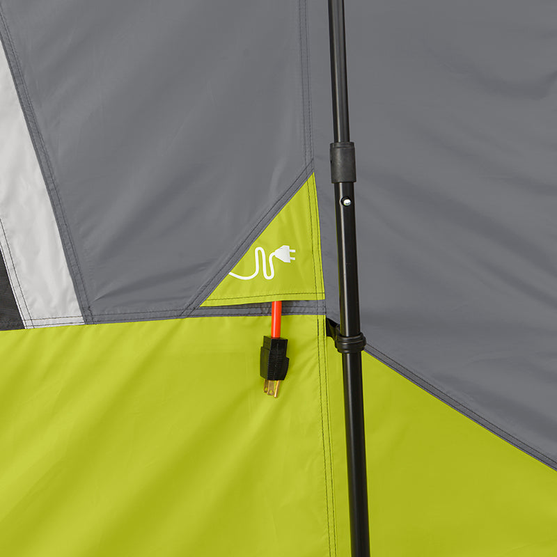 Close-up of an outdoor tent wall featuring a gray and green color scheme. The image highlights an electrical port with a orange power cord plugged into the 9 Person Instant Cabin Tent, alongside a graphic symbol of a plug on the CORE tent fabric. A black tent pole is visible to the right, capturing the essence of camping outdoors.