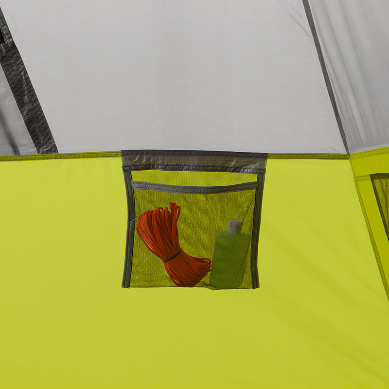 A close-up of a small mesh pocket inside a CORE 9 Person Instant Cabin Tent. The pocket holds a coiled orange rope and a green bottle. The tent fabric is primarily gray with a lime green lower section, perfect for outdoor adventures.