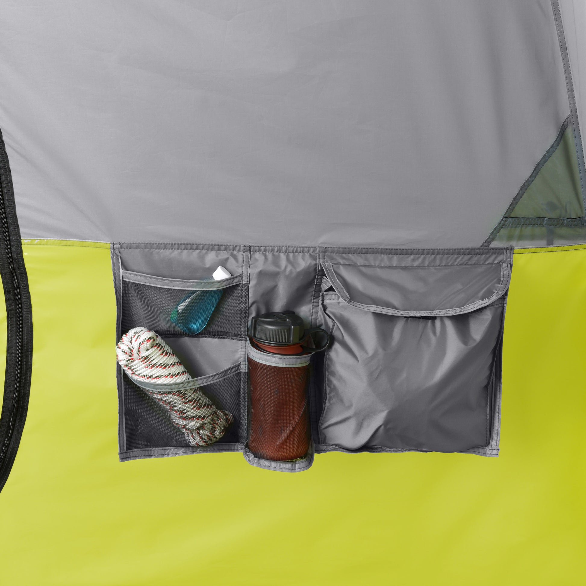 Close-up of a gray and green CORE 10 Person Instant Cabin Tent with Screen Room organizer with multiple pockets. The left pocket holds a coiled rope and a small sanitizer bottle, the middle pocket has a thermos, and the right zippered pocket is partially open, revealing some outdoor essentials inside.