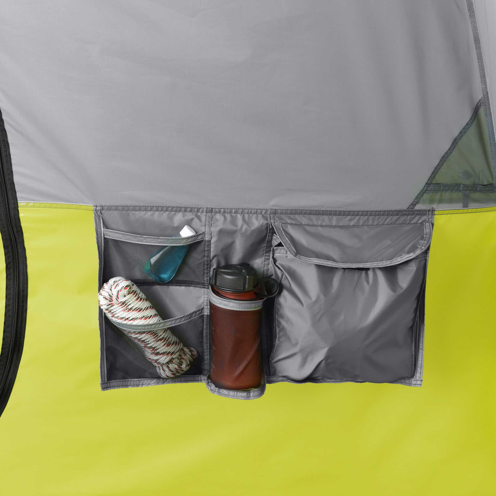 Close-up of a gray and green CORE 10 Person Instant Cabin Tent with Screen Room organizer with multiple pockets. The left pocket holds a coiled rope and a small sanitizer bottle, the middle pocket has a thermos, and the right zippered pocket is partially open, revealing some outdoor essentials inside.