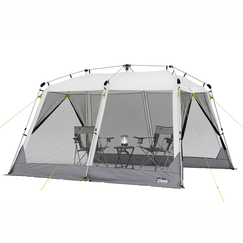 A large, gray rectangular 12' x 10' Instant Screen House with mesh sides and a peaked roof labeled "CORE" is set up with multiple lime green guy lines for stability. Inside are four camping chairs arranged around a small central table with a lantern on it.