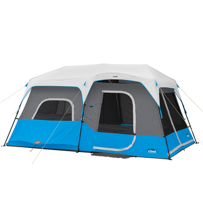 A large, blue and gray CORE 9 Person Lighted Instant Cabin Tent with multiple sections and windows on a white background. The tent features a raised roof, several secured openings for entry and ventilation, and is reinforced with light blue guy lines and stakes for stability.