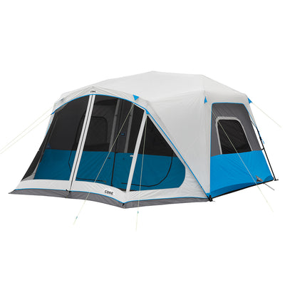 A large, white and blue CORE 10 Person Lighted Instant Cabin Tent with Screen Room with multiple windows and doors is set up with all its guide ropes staked into the ground. Perfect for outdoor adventures, the structure features a vestibule and storage area, with a rainfly that covers the top.