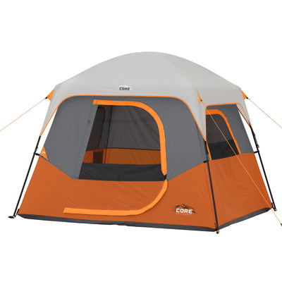 A gray and orange CORE 4 Person Straight Wall Cabin Tent for camping, with a rectangular shape and a front entrance. The tent features mesh windows and a rainfly. It is pitched and secured with guy lines, illustrating a sturdy and spacious design ideal for outdoor use.