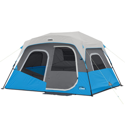 A 6 Person Lighted Instant Cabin Tent with the CORE logo, featuring multiple windows and a large entrance. The tent is set up with steel poles and guylines. It has a rectangular base and a breathable rooftop. Ideal for outdoor activities and group camping trips.