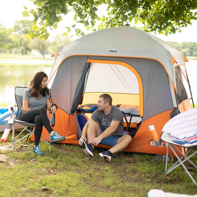 Lifestyle image of couple camping, one sitting in 4 person straight wall tent, one sitting in core camp chair outside of tent