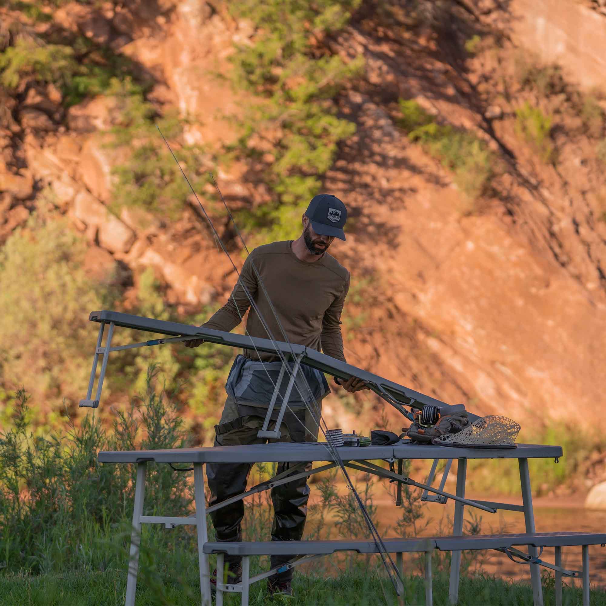 CORE folding picnic table with benches set up outdoors near a rocky hillside.